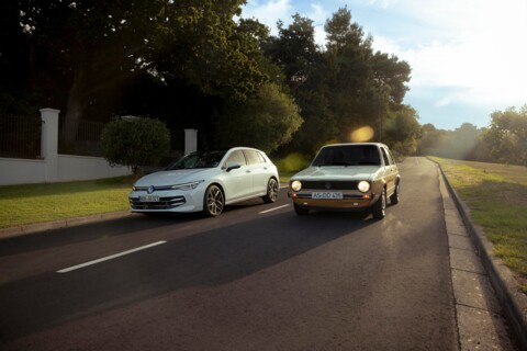 Zwei Volkswagen Golf-Modelle auf einer Landstraße: links ein moderner weißer VW Golf, rechts ein klassischer VW Golf in Beige – Symbol für Tradition und Fortschritt bei Volkswagen.