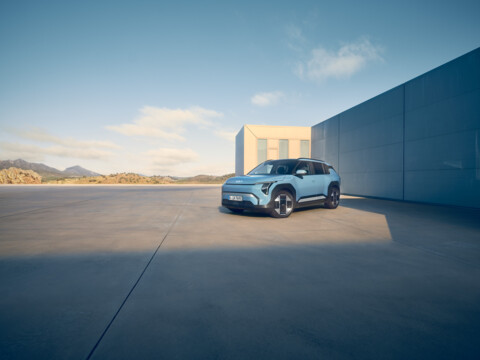 Moderner, blauer Kia Elektro-SUV steht vor einem minimalistischen Gebäude in weiter Landschaft – stilvolle Darstellung moderner Elektromobilität und Design.